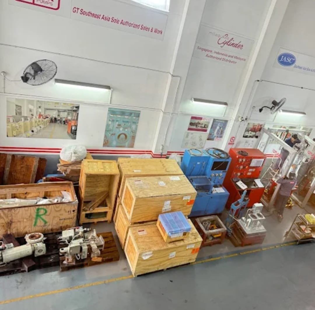 Elevated view of Asia Turbines' Singapore workshop floor with parts crates, control cabinets, and a technician at work